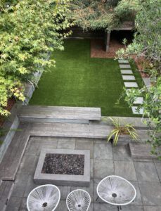 A modern backyard with green lawn, stone steps, and seating area.