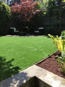 A lush green lawn with garden chairs in the shaded background.