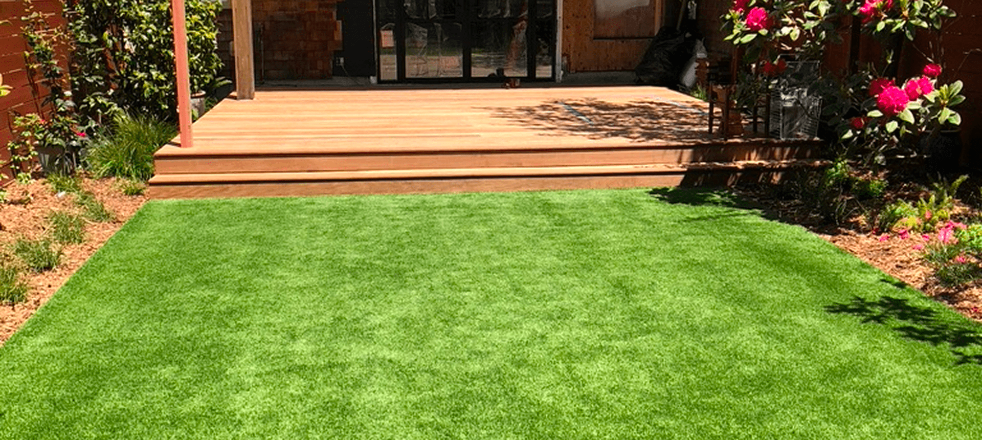 Green lawn with wooden deck and tree shadow in backyard.