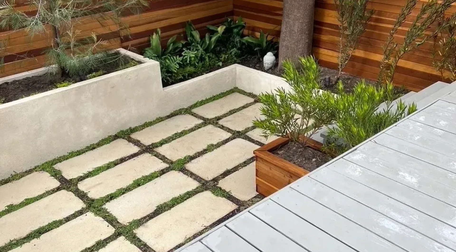 A modern outdoor patio with square stone tiles and greenery.