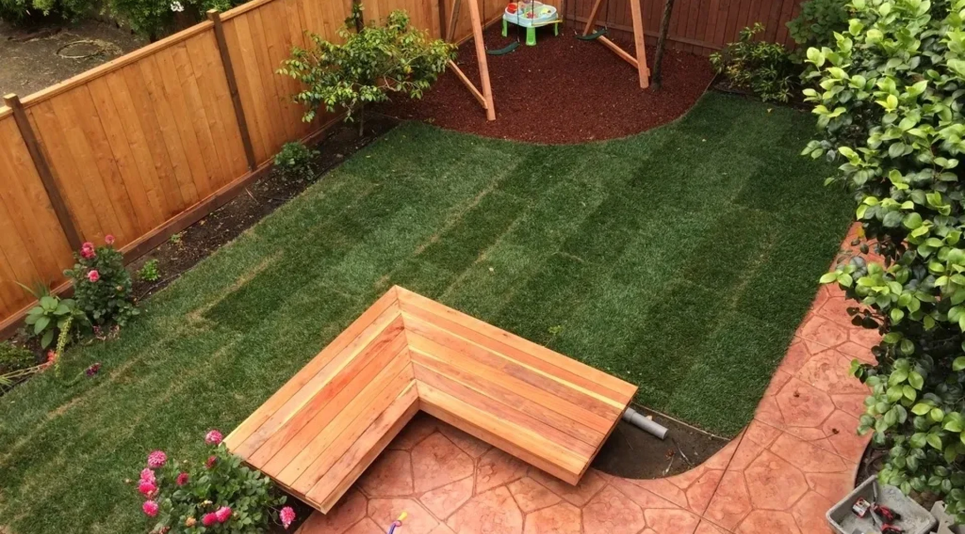 Newly installed striped lawn with wooden corner bench in backyard.