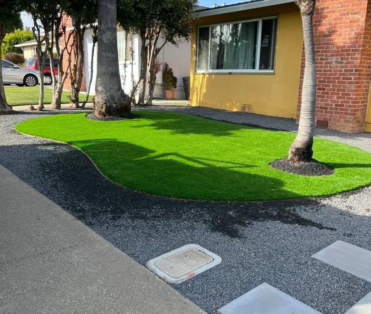 Artificial grass and asphalt near a yellow house with trees.